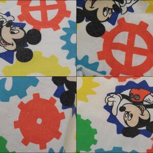 May include: White fabric with a repeating pattern of Mickey Mouse and colourful cogs. Mickey Mouse is shown in different poses within blue starburst shapes. The cogs are red, yellow, blue, and green.