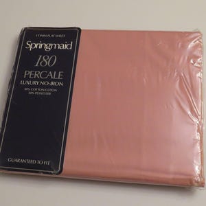 以下が含まれることがあります： 淡いピンク色の新品、未開封のツインフラットシーツ。パッケージには、ブランド名「Springmaid」、糸番手「180」、および「Percale」と「Luxury No-Iron」の文字が記載された濃い青色のラベルが含まれています。シーツはフィットすることが保証されています。