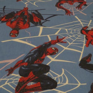 May include: Blue fabric patterned with illustrations of Spider-Man in dynamic poses. The character is shown in his red and black suit, set against a backdrop of white spiderwebs.
