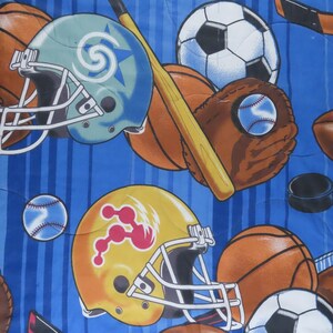 May include: A blue fabric with a repeating pattern of sports equipment. The design includes football helmets, baseballs, basketballs, soccer balls, baseball gloves, hockey sticks, and bats. The background has vertical blue stripes.