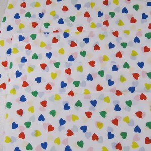 May include: White fabric with a repeating pattern of colorful hearts in red, blue, green, and yellow. The hearts are scattered across the fabric, creating a cheerful and playful design. The fabric appears to be a cotton or similar material.