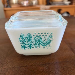 May include: White Pyrex dish with a clear glass lid. The dish features a teal rooster and floral design. The square dish is a vintage kitchenware item.