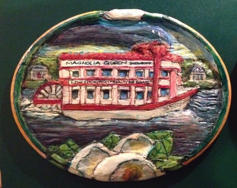 An oval-shaped plaque with wood relief - "Magnolia Queen Showboat" - A unique wood relief carving of an old showboat with a paddlewheel