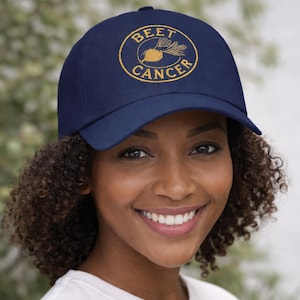 Puede incluir: Gorra de béisbol azul marino con el texto bordado "BEET CANCER" en un diseño circular dorado. La gorra tiene una visera curva y una corona estructurada. El sombrero está hecho de una tela duradera y es adecuado para el uso diario.