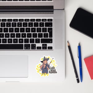 Puede incluir: Una pegatina blanca con una bruja de dibujos animados con pelo rosa, que lleva un sombrero negro y sostiene una varita. La pegatina tiene el texto "Little Witch Academia" y est&aacute; rodeada de hojas amarillas.