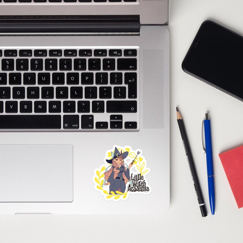 Puede incluir: Una pegatina blanca con una bruja de dibujos animados con pelo rosa, que lleva un sombrero negro y sostiene una varita. La pegatina tiene el texto "Little Witch Academia" y est&aacute; rodeada de hojas amarillas.