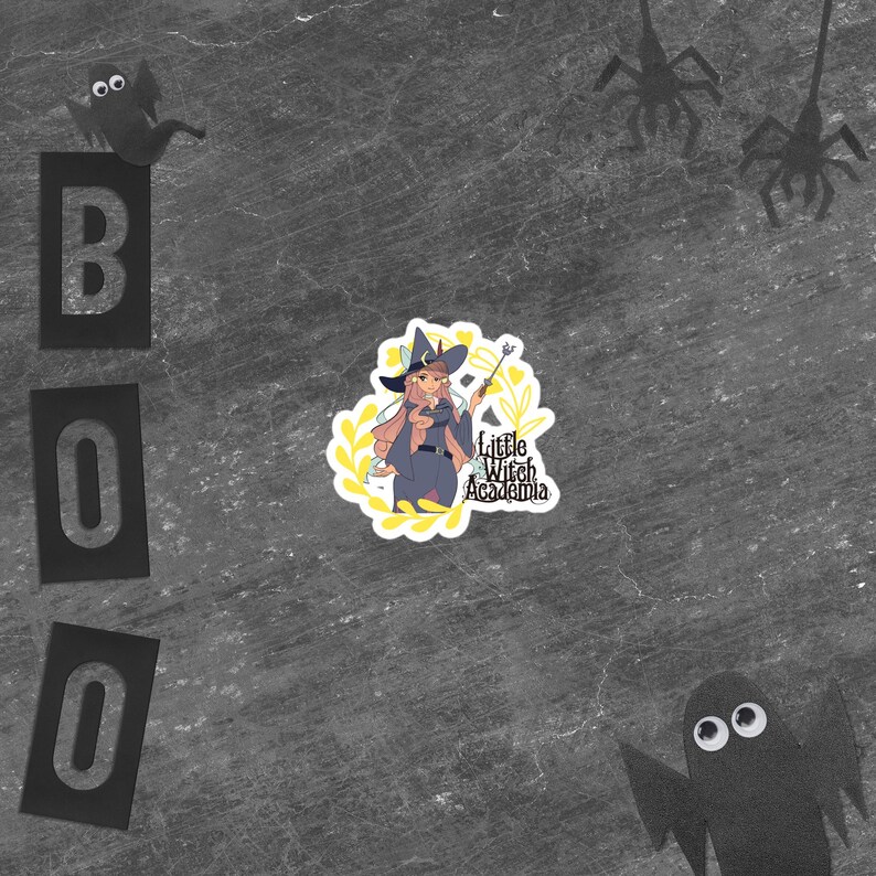 Puede incluir: Una pegatina con una bruja de dibujos animados con pelo rosa, un atuendo azul y una varita m&aacute;gica, rodeada de acentos florales amarillos. La pegatina est&aacute; etiquetada como "Little Witch Academia". La palabra "BOO" est&aacute; escrita con letras negras, y hay recortes de papel de ara&ntilde;as y fantasmas.