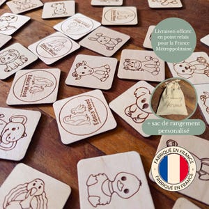 Peut inclure: Jeu de mémoire en bois avec des illustrations d'animaux gravées et le texte "Educa Wood". Comprend un sac en tissu avec le texte "Le memory d'Ariana" et un logo du drapeau français. Les pièces sont carrées et en bois clair.