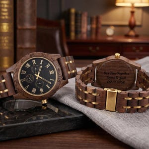 Peut inclure: Deux montres en bois avec des cadrans noirs et des accents dor&eacute;s. L'une affiche l'heure, tandis que l'autre porte l'inscription "Our Time Together, Emma & Jack 02.14.2026" au dos. Les montres sont sur une surface sombre.