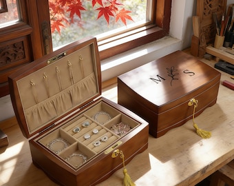 May include: Two wooden jewellery boxes with a dark brown finish. One box is open, revealing a beige velvet interior with necklace hooks, a pocket, and ring slots. The other box is closed, featuring a gold lock with a yellow tassel and the letters M and S.