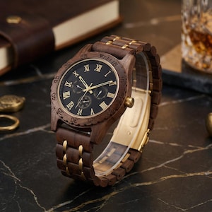 Peut inclure: Une montre-bracelet en bois avec un cadran sombre et des aiguilles et des accents dor&eacute;s. La montre a un bracelet en bois marron avec des maillons dor&eacute;s. Le cadran de la montre comporte des chiffres romains. La montre est pr&eacute;sent&eacute;e sur une surface sombre.