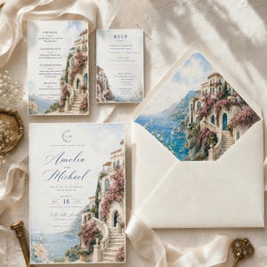May include: A wedding stationery set featuring a watercolor illustration of a coastal Italian villa with pink flowers, blue sea, and stone stairs. Includes a main invitation for Amelia and Michael, an RSVP card, and an envelope with a matching liner.