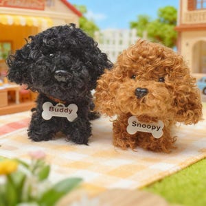 May include: Two toy poodle plushies, one black and one brown, are positioned together on a checkered surface. The black poodle wears a bone-shaped tag that reads "Buddy", while the brown poodle's tag says "Snoopy".