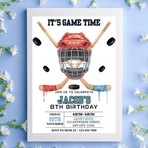 May include: A framed invitation for Jacob's 8th birthday, featuring a hockey theme. The design includes a red hockey helmet, crossed hockey sticks, and pucks. Text reads "IT'S GAME TIME" and details of the party.