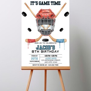 May include: A hockey-themed birthday party invitation on an easel. The invitation features a red hockey helmet, crossed hockey sticks, and black pucks. Text includes "IT'S GAME TIME" and details for Jacob's 8th birthday.