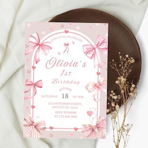 Puede incluir: Una invitación de cumpleaños rosa y blanca con el texto "Olivia's 1st Birthday". La invitación presenta lazos rosas, corazones y detalles florales. La fecha es el 18 de octubre a las 4 PM. Incluye dirección e información RSVP.
