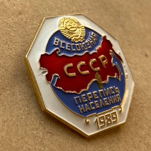 May include: A hexagonal metal pin featuring a white border, a blue background, and a red map silhouette. The pin displays the gold text CCCP, the Cyrillic text ВСЕСОЮЗНАЯ ПЕРЕПИСЬ НАСЕЛЕНИЯ, the year 1989, and a gold emblem of a hammer and sickle.
