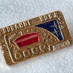 Könnte beinhalten: Vintage rechteckige Anstecknadel mit goldfarbenem Metall und Emaille-Details. Die Anstecknadel zeigt ein rotes und blaues Design mit kyrillischem Text und den Buchstaben "CCCP". Die Anstecknadel hat einen strukturierten Rand und ist wahrscheinlich ein Sammlerstück.