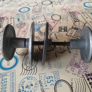 May include: A gray metal door handle assembly featuring two circular plates and two cylindrical grips connected by a central metal rod. The hardware has a matte finish and a simple, functional design with visible screw threads on the connecting rod.