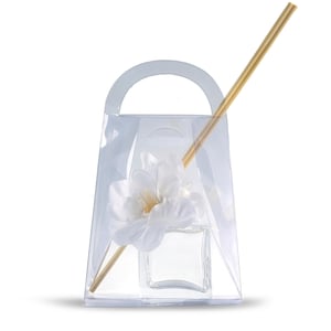 May include: A clear, square glass diffuser bottle with a white flower and wooden reeds, presented in a clear plastic bag with a handle. The reeds are angled, and the flower is in the center of the bottle.