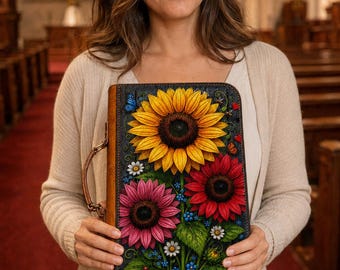 May include: A rectangular leather-bound book cover featuring a vibrant embossed design of large yellow, red, and pink sunflowers with green leaves, small blue flowers, and tiny butterflies against a dark background, complete with a side handle.