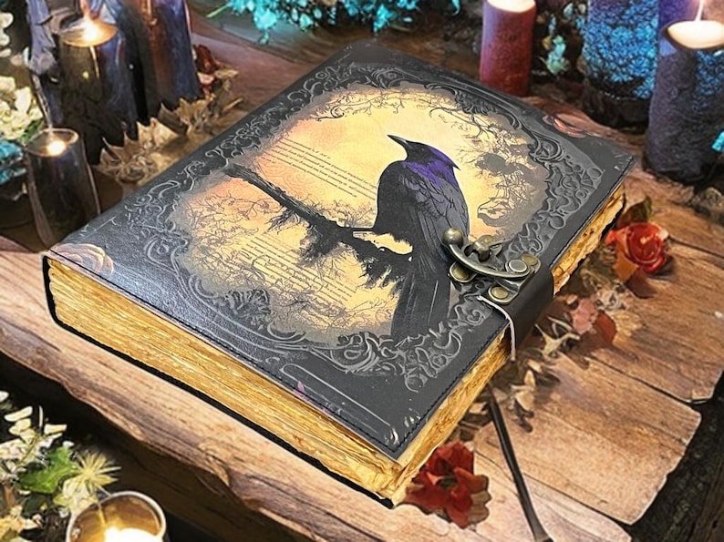 May include: A leather-bound journal with a raven illustration. The cover features a black raven perched on a branch against a yellowed background with musical notes. The edges of the pages are gold, and the journal is secured with a metal clasp.