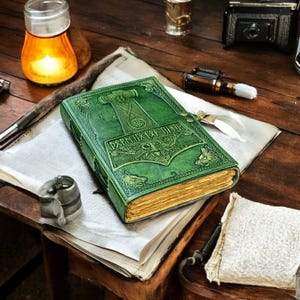May include: A green leather-bound journal with embossed Norse designs, including a hammer and wolf figures. The journal has gold-edged pages and a clasp closure. The cover features runic text. The journal rests on a vintage wooden surface.