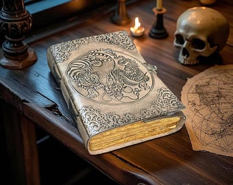 May include: A detailed, antique-style journal with a silver cover featuring a tiger and dragon design. The book has gold-edged pages and a clasp closure. The journal is on a dark wooden surface, with candles and a skull in the background.