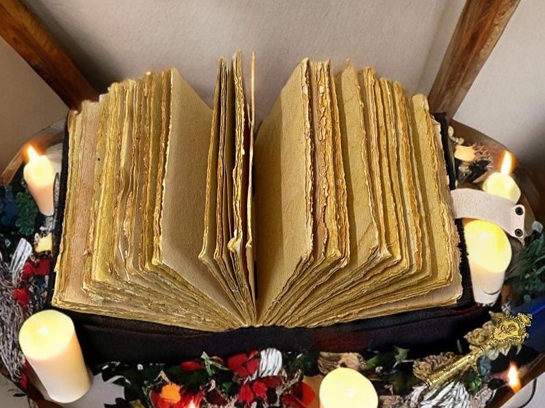 Puede incluir: Un libro abierto y envejecido con p&aacute;ginas gruesas y amarillentas. El libro est&aacute; rodeado de velas encendidas y elementos decorativos. Las p&aacute;ginas tienen un aspecto rugoso y texturizado, lo que sugiere edad y uso. La est&eacute;tica general es vintage y m&iacute;stica.