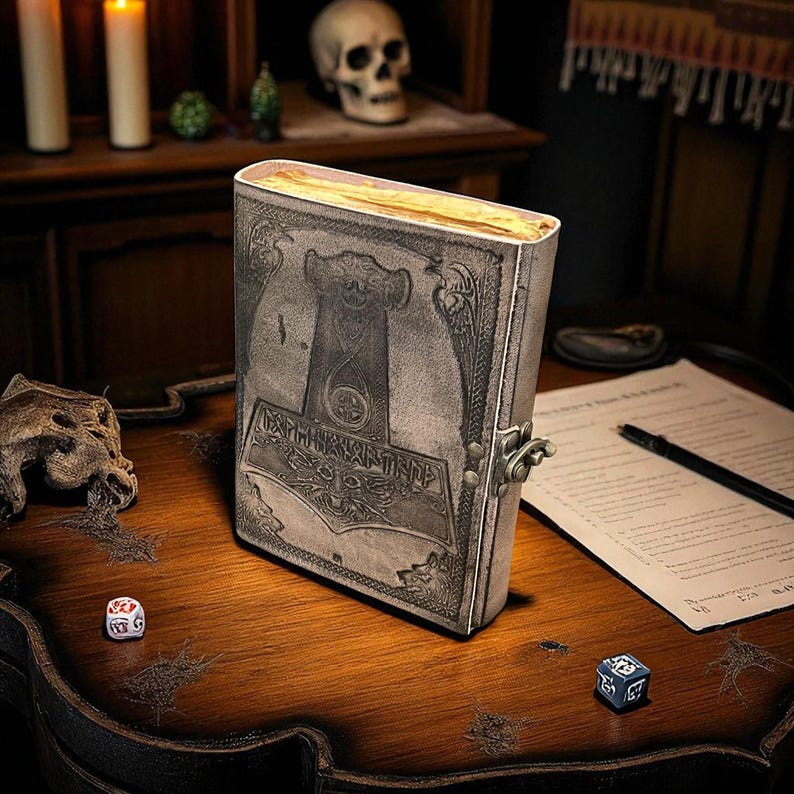 May include: A leather-bound journal with a metal clasp, featuring an embossed design of a hammer and runes. The journal is open, revealing aged pages. The scene includes dice, a pen, and a skull, suggesting a fantasy or historical theme.