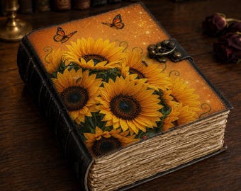 May include: A hardcover journal featuring a vibrant illustration of yellow sunflowers and orange butterflies on an amber background. The book has a dark, textured spine, a metallic latch closure, and thick, deckled-edge paper pages.
