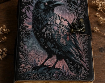 May include: A rectangular journal with a black cover featuring a detailed illustration of a raven surrounded by botanical elements, ferns, and a crescent moon. The book includes a metal latch closure and has thick, aged-looking paper pages.