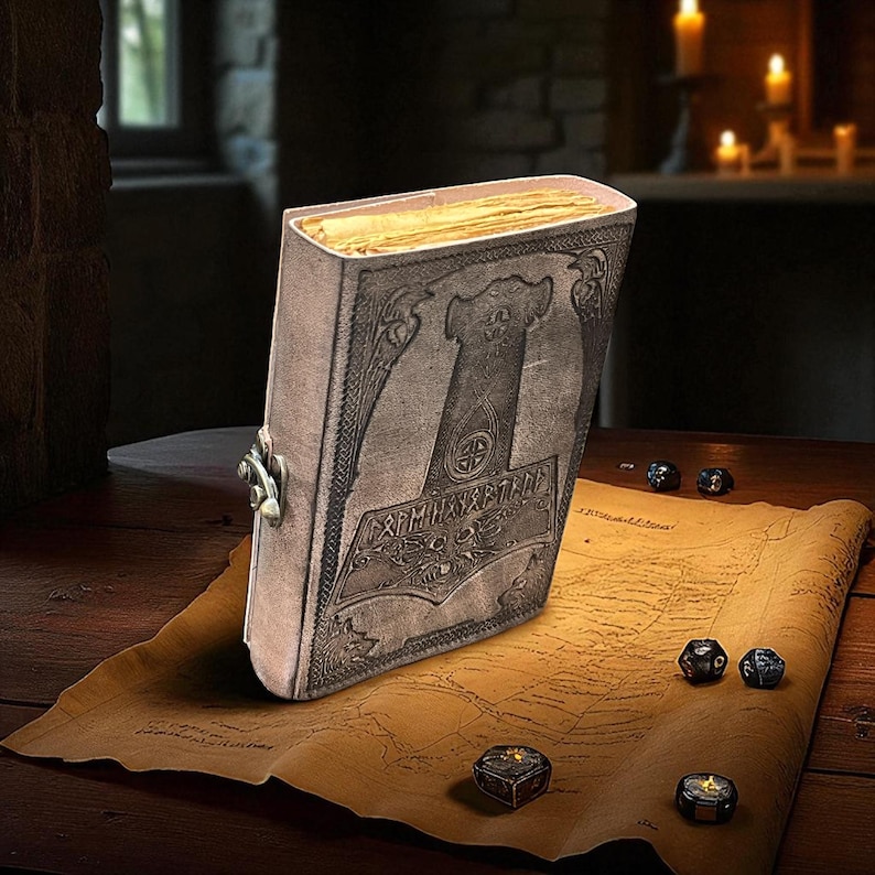 May include: A leather-bound journal with an embossed design featuring a hammer and runic text. The journal is closed with a metal clasp and rests on a parchment map. Dice and a small box are scattered around the map.
