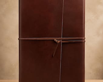 May include: A rectangular dark brown leather journal with a smooth, matte finish. The cover features a wrap-around design secured by a thin leather cord tied in a simple knot at the front center, keeping the notebook closed securely.