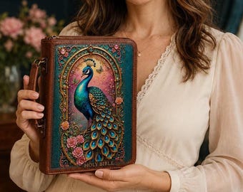 May include: A brown leather-bound Holy Bible featuring a rectangular front cover with a teal border and an ornate central illustration of a peacock surrounded by pink roses and gold filigree details, including a side handle and zipper closure.
