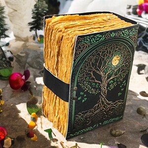 Puede incluir: Un diario hecho a mano con una cubierta negra con un dise&ntilde;o de &aacute;rbol de la vida en dorado y verde. Las p&aacute;ginas son de color dorado texturizado, encuadernadas con una correa negra. Un art&iacute;culo art&iacute;stico &uacute;nico.