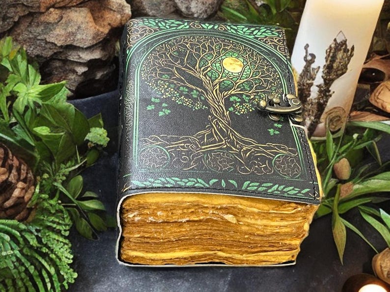 Puede incluir: Un diario encuadernado en cuero con un dise&ntilde;o de &aacute;rbol de la vida en la portada. La portada es negra con detalles verdes y dorados. Las p&aacute;ginas est&aacute;n envejecidas y amarillentas, y el diario tiene un cierre met&aacute;lico.