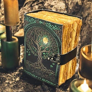 Puede incluir: Un diario encuadernado en cuero con un dise&ntilde;o de &Aacute;rbol de la Vida en la portada. La portada es negra con detalles verdes y dorados. Las p&aacute;ginas envejecidas se sujetan con una correa de cuero negro. Velas y candelabros en el fondo.