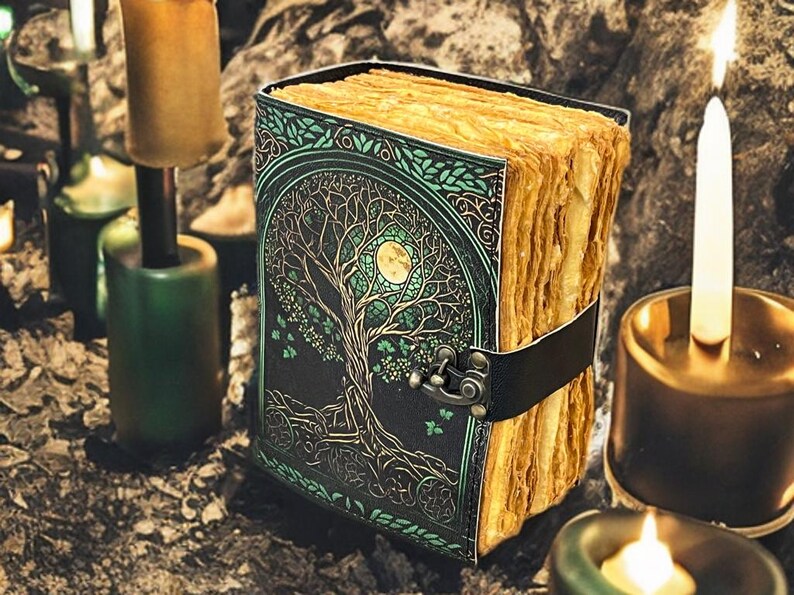 Puede incluir: Un diario encuadernado en cuero con un dise&ntilde;o de &Aacute;rbol de la Vida en la portada. La portada es negra con detalles verdes y dorados. Las p&aacute;ginas envejecidas se sujetan con una correa de cuero negro. Velas y candelabros en el fondo.