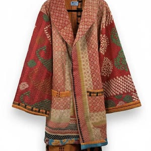 Puede incluir: Una chaqueta larga y abierta con un diseño de patchwork en tonos rojos, naranjas y beige. La chaqueta presenta un cuello chal, dos bolsillos delanteros y diversos paneles de tela estampada. Las mangas son anchas y la chaqueta llega hasta la pantorrilla.