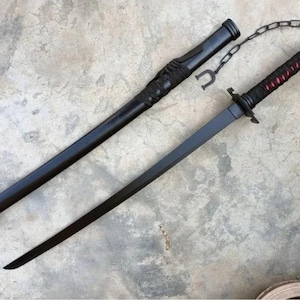 May include: A black katana sword with a matching scabbard. The handle is wrapped in black fabric with red accents. A chain connects the scabbard to the handle. The blade is straight and black.