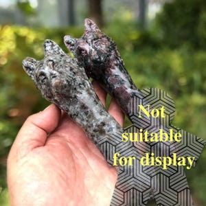 May include: Two carved stone wolf head sculptures. One is gray with black speckles, the other is dark red with black and white speckles. The text "Not suitable for display" is overlaid on the image.