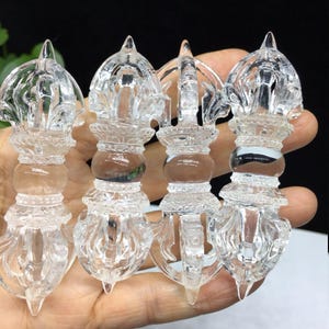 Peut inclure: Quatre sceptres Vajra en cristal clair, chacun avec un design détaillé et orné. Les sceptres ont une colonne centrale avec une section bulbeuse et une pointe. Le cristal est transparent, permettant à la lumière de passer, et l'effet global est celui d'un artisanat complexe.