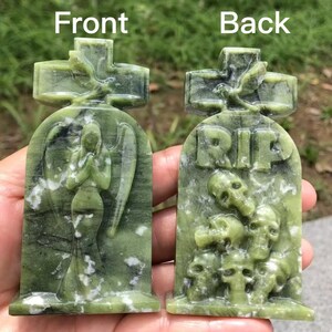 May include: A green stone tombstone with a cross on top. The front features an angel statue, while the back has the letters "RIP" above skulls. The stone has a marbled appearance.