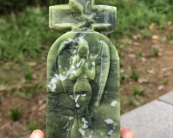 May include: A green stone sculpture of an angel with outstretched wings, hands clasped in prayer, and a cross at the top. The angel is carved in detail, with a flowing gown. The stone has white and black veining.
