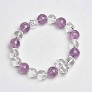 May include: A beaded bracelet featuring alternating round, translucent quartz and purple amethyst stones. The bracelet is strung together with a clear elastic cord, creating a stretchable design. The beads are approximately 1 cm in diameter.