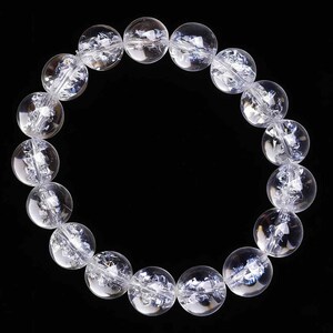May include: A clear quartz crystal bead bracelet. The bracelet features large, round, transparent beads with internal fractures, strung together on a clear elastic cord. The beads are approximately 1 inch in diameter. The background is solid black.
