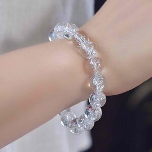 May include: A stretch bracelet composed of round, clear, crackled glass beads. Each bead features an internal fractured texture that catches the light, creating a shimmering, translucent appearance throughout the circular accessory.
