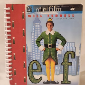Puede incluir: Un DVD de la película "Elf" con Will Ferrell y James Caan. La portada muestra a Ferrell con un disfraz de elfo contra un paisaje urbano. El DVD está encuadernado con un cuaderno de espiral con una cubierta roja decorada con árboles de Navidad.