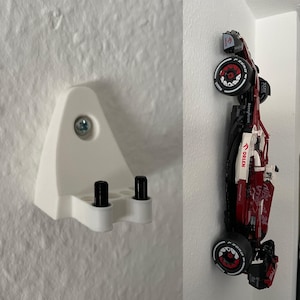 Könnte beinhalten: Eine weiße Wandhalterung mit zwei schwarzen Stiften und einer silbernen Schraube, die ein rotes und schwarzes Rennwagenmodell hält. Das Auto trägt die Aufschrift "ORLEN" und "P ZERO".